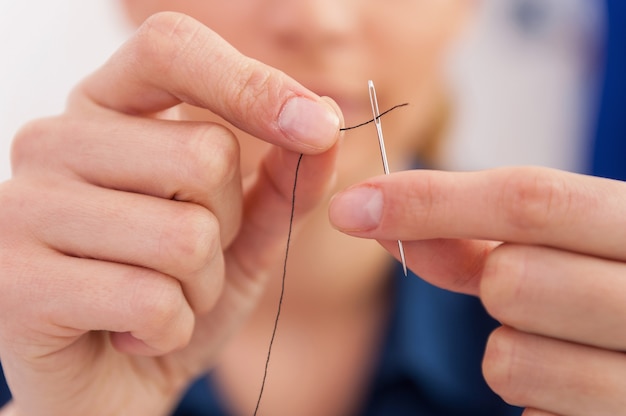 Infilare nell'ago. primo piano della donna che tira il filo nell'ago