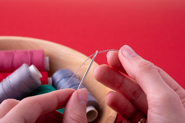 Thread into needle process woman hands on red wall