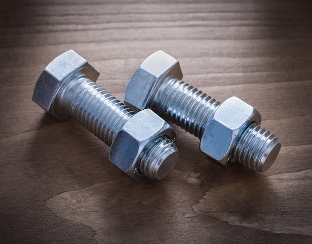 Threaded bolts and nuts on wooden surface construction concept.