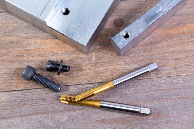 Threaded steel billet, hex bolt and metal taps on wood board. Tool for metal processing.