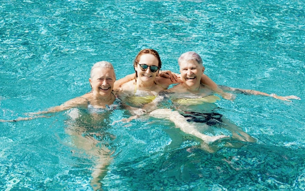 Three active mature senior caucasian friends women have fun in outdoor swimming pool under the sun