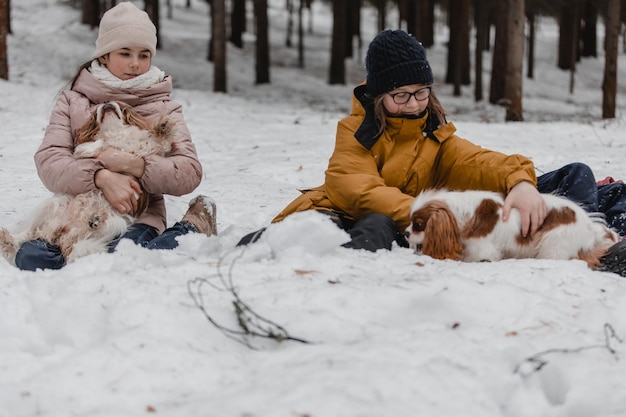 Three adorable young girls having fun together by beautiful frozen park forest Cute sisters playing in a snow with a dog