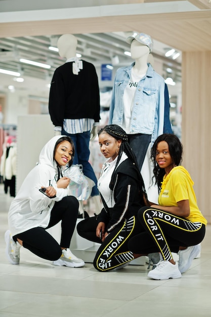 Three afican american women in tracksuits shopping at\
sportswear mall against mannequin sport store theme