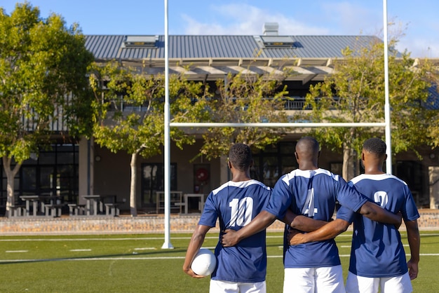 Foto tre giovani atleti maschi afroamericani con una palla da rugby in piedi su uno spazio di copia di campo