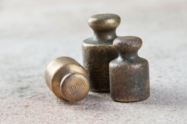 Three antique bronze weights for scales on concrete.