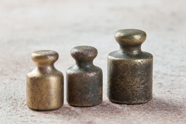 Three antique bronze weights for scales on concrete.