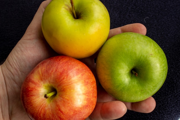 В руке три яблока, одно зеленое и два красных и желтых.