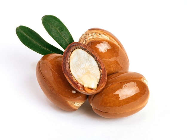 Photo three argan nuts with green leaves on an isolated white background chopped argan nut with a drop of