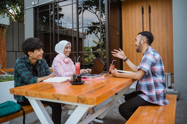 Three asian college students sitting chatting in a cafe when they meet