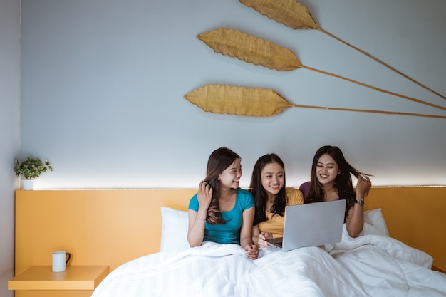 Tre ragazze asiatiche che utilizzano computer portatile insieme su un letto in camera da letto