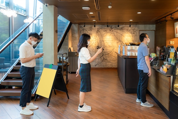 Three Asian people wearing mask standing distance of 6 feet from other people keep distance protect from COVID-19 viruses and people social distancing for infection risk at coffee cafe.
