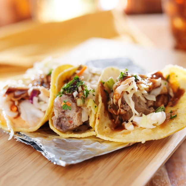 Three asian pork tacos on a wooden board