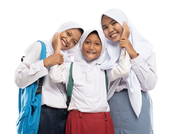 Three asian in veils in school uniforms stand smiling with affectionate gestures of each other while...