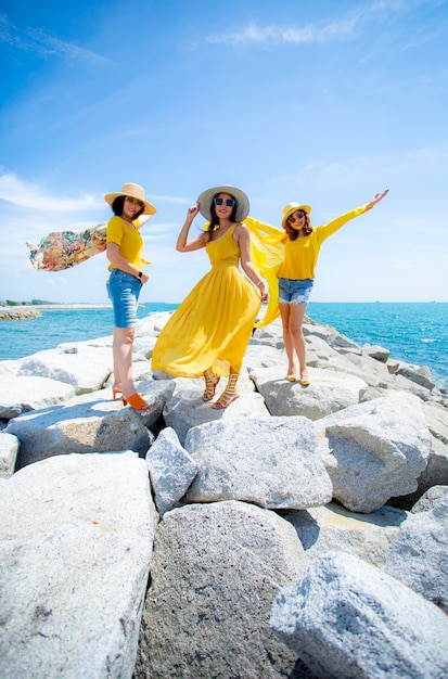 La donna asiatica tre che indossa i vestiti gialli che stanno sul mare tira contro la luce del sole di mezzogiorno