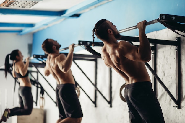 Three attractive young male and female adults doing pull ups on bar