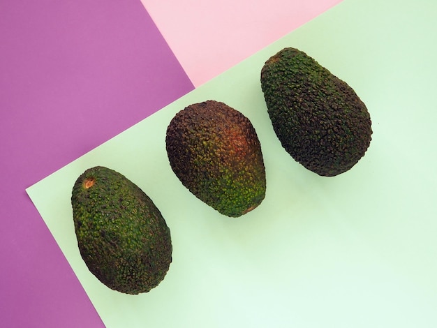 Three avocados of different ripening stages on light green pink and purple geometric background