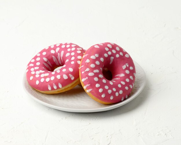 Three baked round donuts in a white round ceramic plate, close up