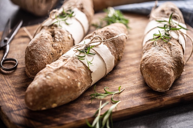 Three baked whole wheat baguette breads with rosemary in a rustic wooden environment