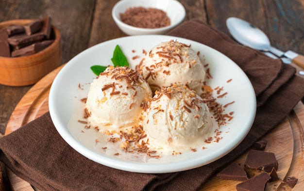 Three balls of ice cream close-up in a white plate on a brown wall. Side view, horizontal. Summer dessert.