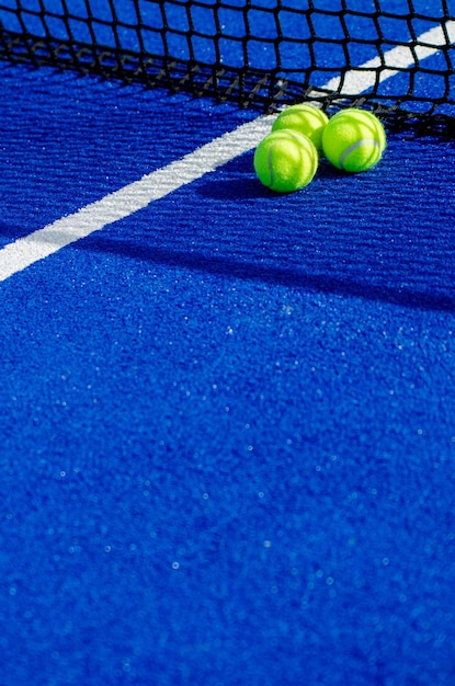 Three balls near the net of a blue padel tennis court racket sports concept