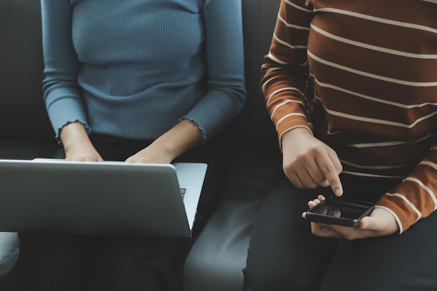 Three beautiful Asian girls using smartphone and laptop chatting on sofa together at cafe with copy space modern lifestyle with gadget technology or working woman on casual business concept