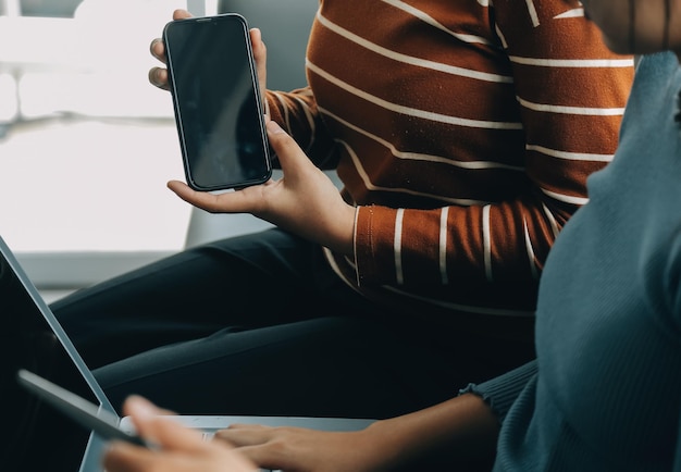 Three beautiful Asian girls using smartphone and laptop chatting on sofa together at cafe with copy space modern lifestyle with gadget technology or working woman on casual business concept