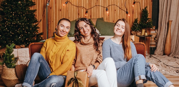 Three beautiful cheerful happy young girls girlfriend give Christmas gifts on the of a new year tree at home