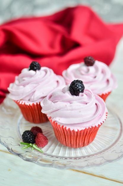 Three beautiful cupcakes with pink cream, with fresh raspberries and blackberries