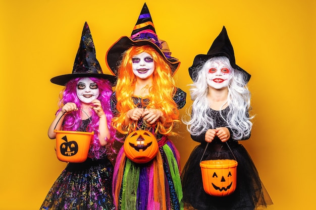 Three Beautiful girls in a witch costumes and hats on a yellow background scaring and making faces.