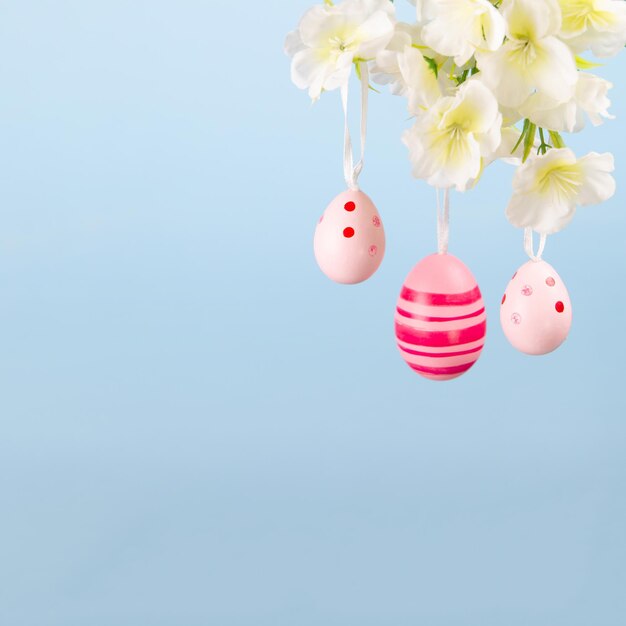 Three beautiful pink Easter eggs hanging from a flowering branch on a serene blue backdrop