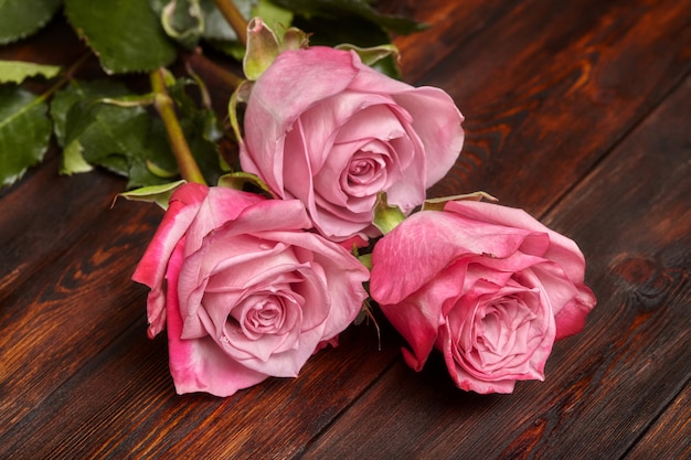 Three beautiful pink roses on wooden table, romantic wall