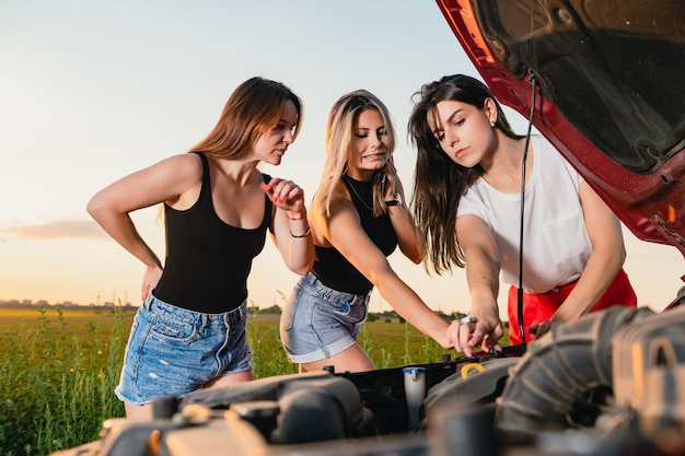 Three beautiful women stuck during road trip, try to fix vehicle, looking at open hood, driving adventures