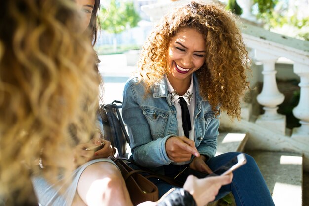 Three beautiful young women using they mobile phone in the street.