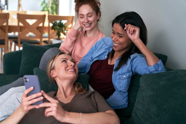 3人の白人の親友がソファでスマートフォンをブラウジングしながら微笑んでいる