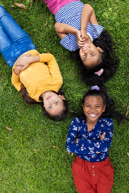 Three biracial girls are lying on the grass in school smiling and looking upwards