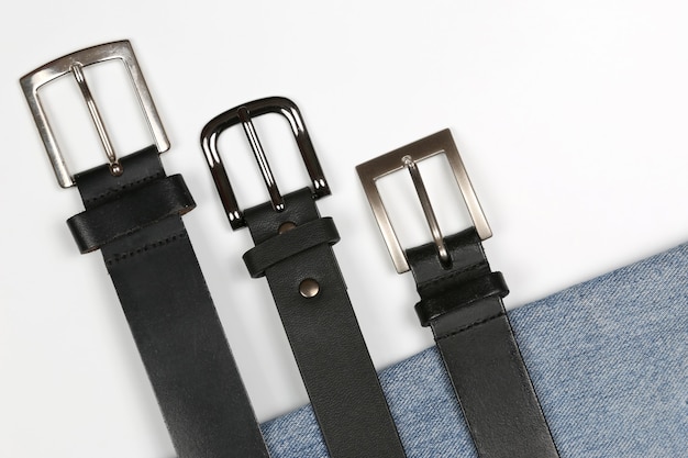 Photo three black leather belt on a white surface with jeans