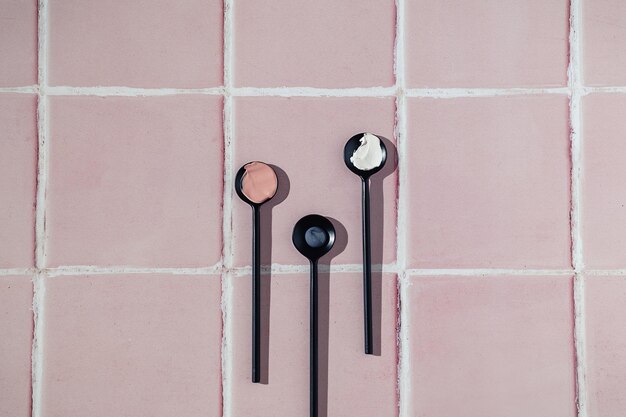 Three black spoons with cream smear or black and white mud mask
smudge texture on pink tile bathroom floor bathroom with copy
space. natural beauty skin care cosmetic product. flat lay. facial
spa.