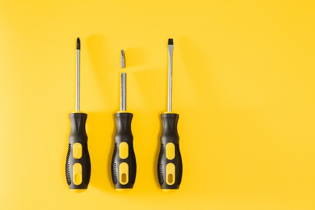 Three black and yellow screwdrivers on a yellow background with space for text. Tools, construction and workshop, home repairs, slusar work.