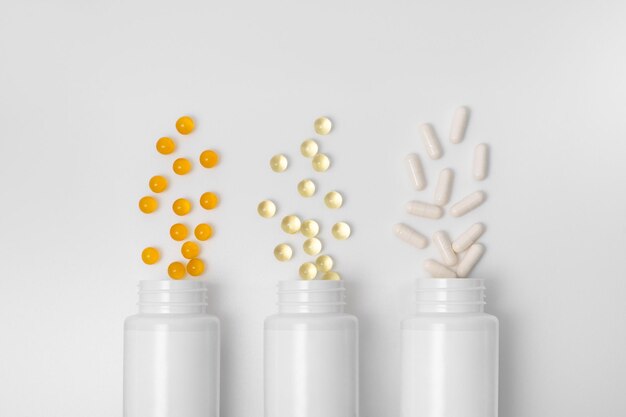 Three blank jars with yellow orange and white capsules pills on a gray isolated background Concept of health medicines and pharmacy Image for your design