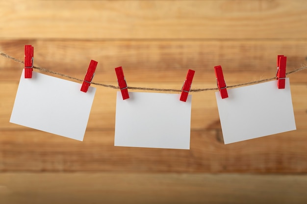 Three blank white paper cards hanging with clothespins on rope string peg on wooden background. Copy space.