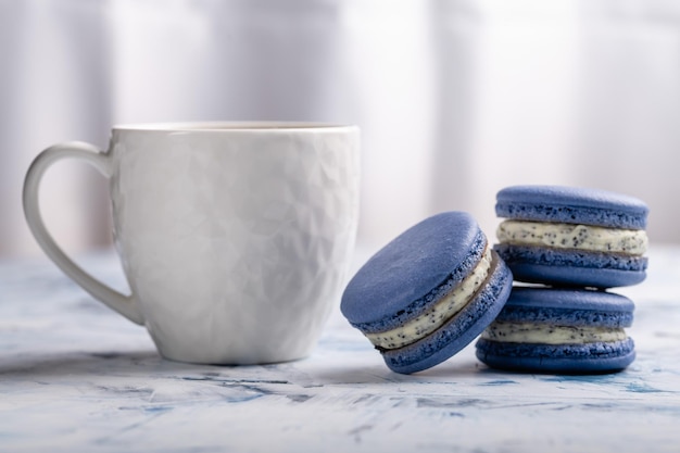 Three blue macaroons and a white cup on a light background