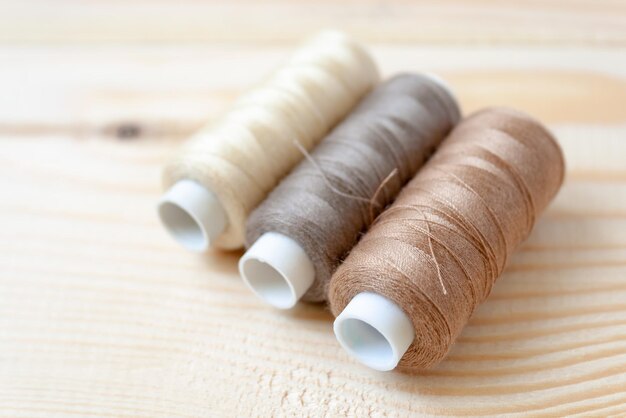 Three bobbins of threads of brown shades lie on a wooden background