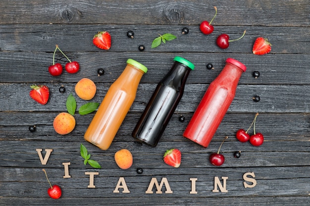 Three bottles of juice, fruit and inscription Vitamins. Wooden background.