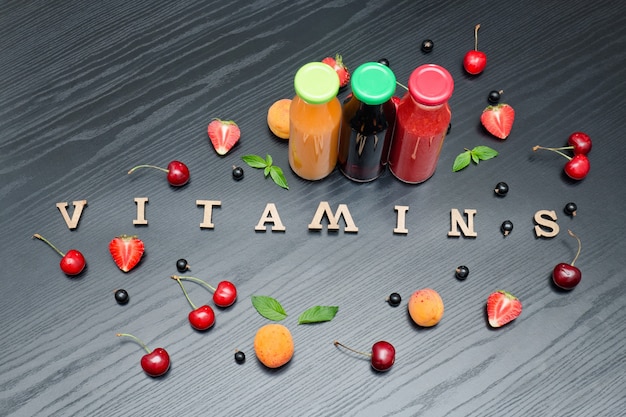 Three bottles of juice, the inscription Vitamins and fruits. Wooden background.