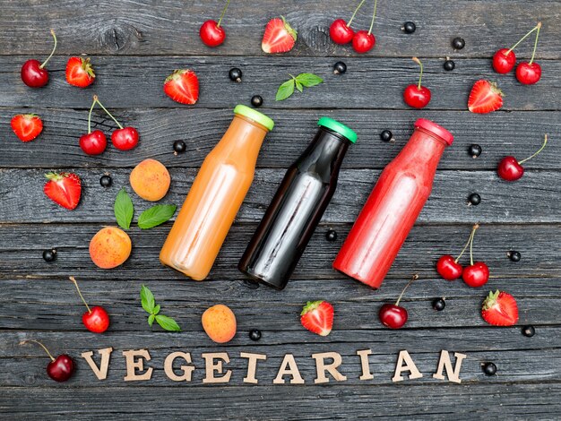 Three bottles with juice, fruit and inscription Vegetarian on black wooden background. Food concept