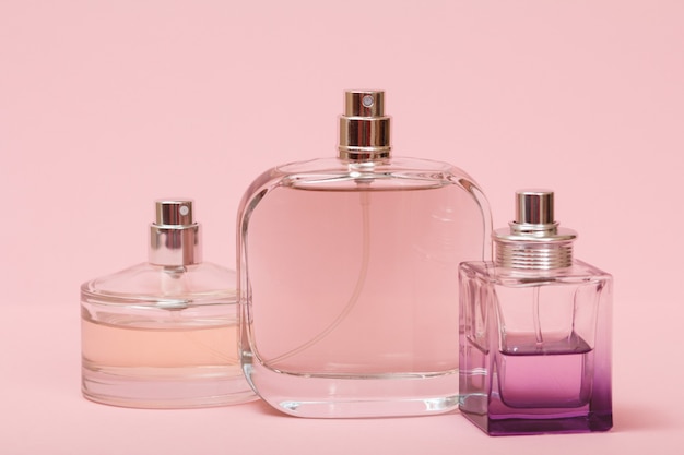 Three bottles with women perfume in a pink background. Women products.