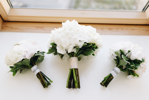 Three bouquets of white hydrangea lay flat on the window-sill top-down 