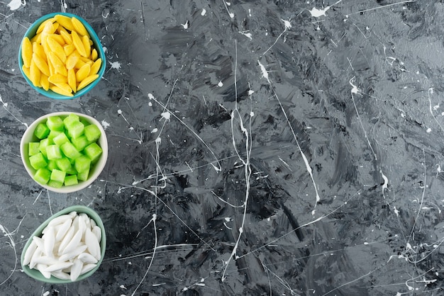 Three bowls full of colorful sweet candies on a marble surface