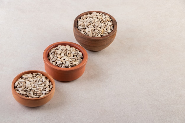 Three bowls of organic sunflower seeds placed on stone table.