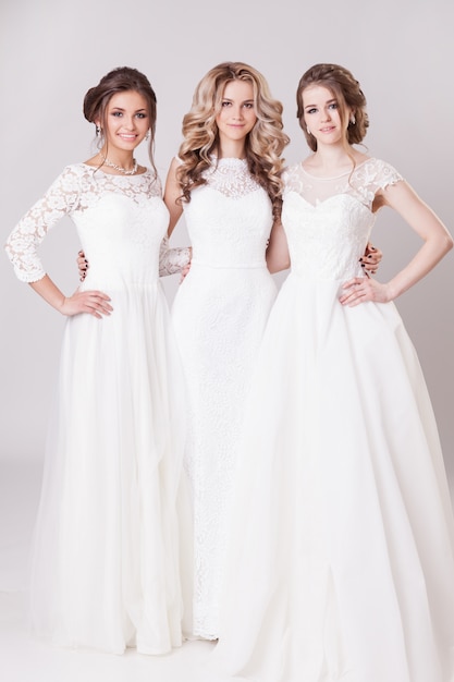 Three the bride with beautiful hair and makeup posing and hugging in the Studio. In wedding dresses